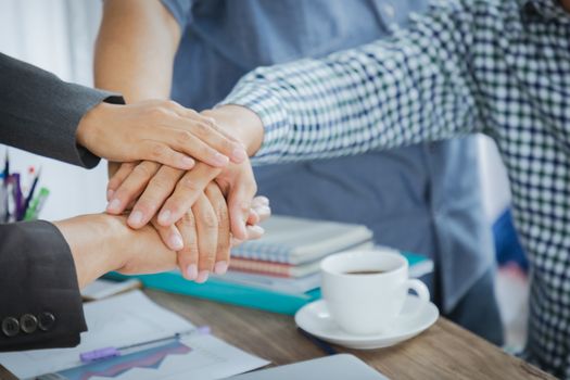 Business people man and women putting their hands group together. On the desk office table in the meeting room of the workplace.