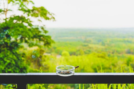 Smoking cigarette is not good for health in ashtray on the balcony. Tree and Forest, mountain and nature background.