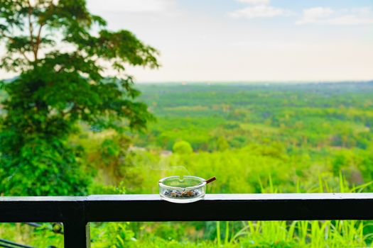 Smoking cigarette is not good for health in ashtray on the balcony. Tree and Forest, mountain and nature background.