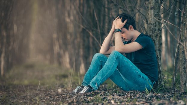 Unhappy man in the forest suffers from depression and frustration of life.