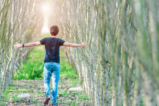 happy man running on a forest path opposite the sun. hands touching a tree branch.