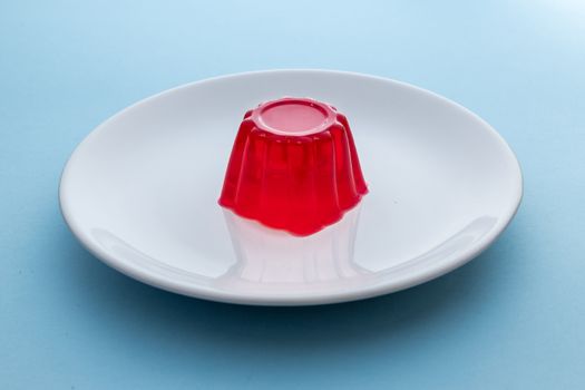 Close-up of a strawberry jelly dessert on a white plate with a light blue background