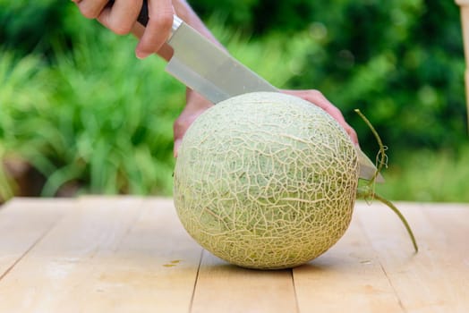 The man use knife split the orange melon on wood plate