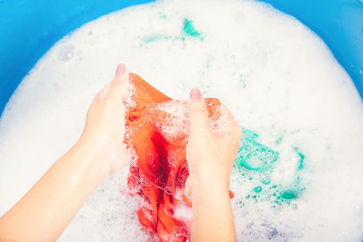 Closeup young Asian woman use hands washing color clothes in basin with detergent have soapy bubble water, studio shot background, laundry concept