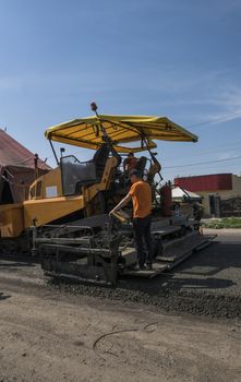 Worker operating asphalt paver machine during road construction and repairing works. A paver finisher, asphalt finisher or paving machine placing a layer of asphalt. Repavin