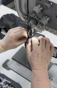 Sewing machine in a leather workshop in action with hands working on a leather details for shoes. Old women's hands with sewing machine at shoes factory