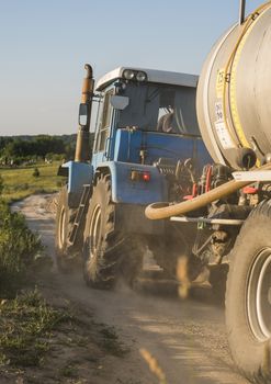 A blue tractor with a tank rides along a road in a wheat field