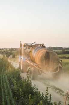 A blue tractor with a tank rides along a road in a wheat field