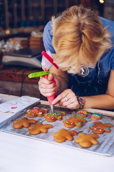 Unrecognizable women confectioner hand decorating a gingerman with a pastry bag, drawing a smile, making it cute, fun and delicious. Woman making ginger bread cookies in the kitchen.