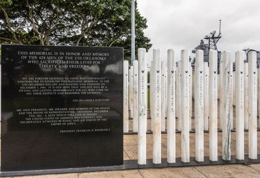 Oahu, Hawaii, USA. - January 10, 2020: Pearl Harbor, Group of white name sticks and black marble slab with texts at USS Oklahoma memorial. Green foliage and gray sky in back.