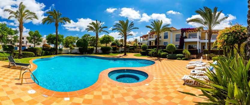 Swimming pool, sun-loungers and palm trees during a warm sunny day, paradise destination for vacations. Backyard swimming pool with garden full of palm trees and flowers. Backyard with swimming pool.