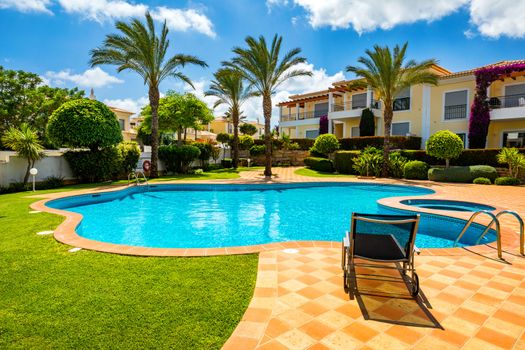 Great backyard with swimming pool, hot tub and lounge chairs. Swimming pool in backyard. Incredible swimming pool and garden with palm trees and flowers in a sunny day.