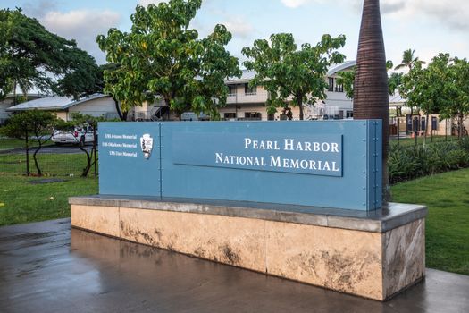 Oahu, Hawaii, USA. - January 10, 2020: Pearl Harbor National Memorial welcome sign has white letters on blue background under white cloudscape with green lawn in back. Some low level buildings.