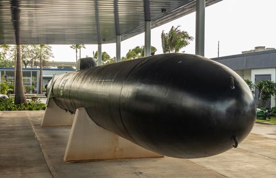 Oahu, Hawaii, USA. - January 10, 2020: Pearl Harbor. Big black One-man Japanese suicide or Kamikaze torpedo, called Kaiten, under gray metal roof. Green foliage in back.