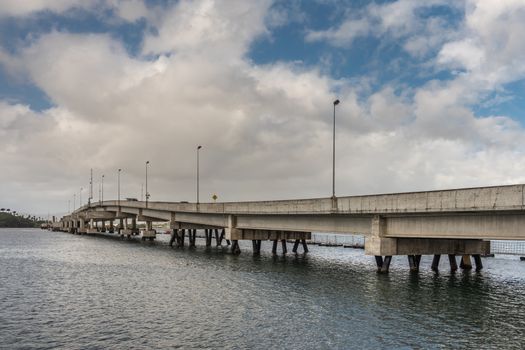 Oahu, Hawaii, USA. - January 10, 2020: Pearl Harbor. Ford Island pontoon bridge froms beige concrete line between gray water and blue cloudscape.