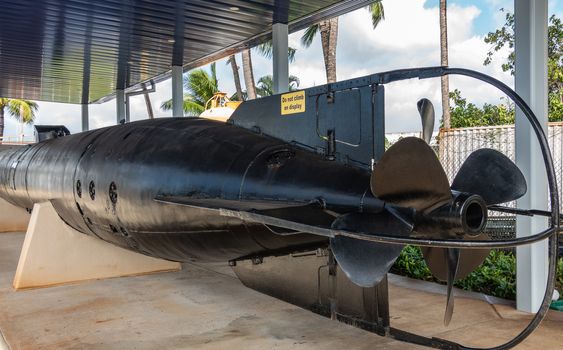 Oahu, Hawaii, USA. - January 10, 2020: Pearl Harbor. Big black One-man Japanese suicide torpedo, called Kaiten, seen from stern, under gray metal roof. Green foliage in back.