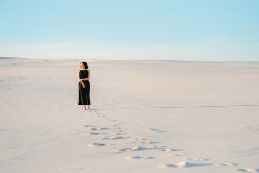 girl in a black dress stands in the middle of the desert against the background of footprints