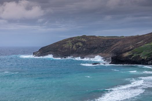 Oahu, Hawaii, USA. - January 11, 2020: Hanauma Bay Nature Preserve. White waves of azure water run along cliffs with face of baboon under heavy rain cloudscape.