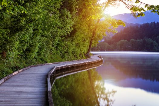 Wooden walkway around the lake Bled with mountains and houses on the background. Beautiful Slovenian Nature. Bled, Slovenia, Europe. 