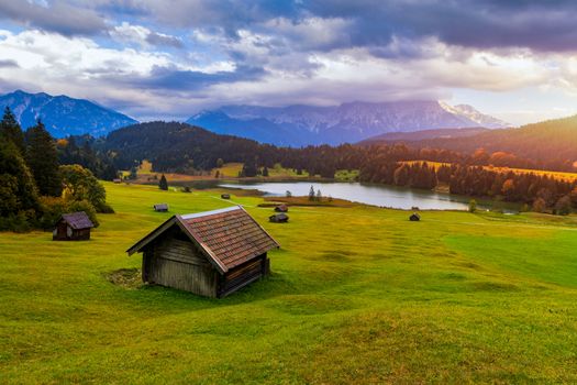 Panoramic morning scene of Wagenbruchsee (Geroldsee) lake with Zugspitze mountain range on background. Amazing autumn view of Bavarian Alps, Germany, Europe. Wooden hut on meadow by Geroldsee lake. 
