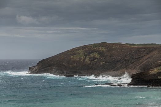 Oahu, Hawaii, USA. - January 11, 2020: Hanauma Bay Nature Preserve. Baboon face cliff sits at entrance of bay with greenish water. Darker ocean water behind and very heavy dark cloudscape.