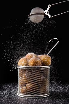 Pouring sugar on Carnival fritters or buñuelos de viento for holly week on black background