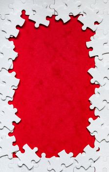 Framing in the form of a rectangle, made of a white jigsaw puzzle. Frame text and jigsaw puzzles. Frame made of jigsaw puzzle pieces on red background.