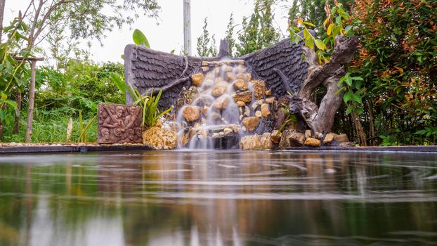 Fish pond with waterfall fountain. Garden waterfall landscaping with fishes, rocks, flowers and plants.