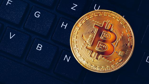 Bitcoin on compuer keyboard in background, symbol of electronic virtual money and mining cryptocurrency concept. Coin crypto currency bitcoin lies on the keyboard. Bitcoin on keyboard.