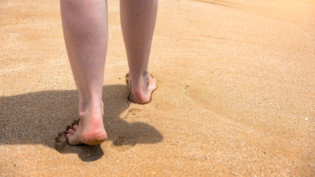 Woman walking barefoot on a beach. Close up leg of young woman walking along wave of sea water and sand on the summer beach. Travel Concept. Woman walking on sand beach leaving footprints in the sand.