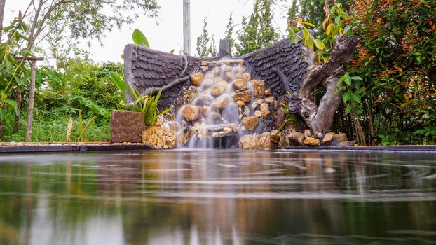 Fish pond with waterfall fountain. Garden waterfall landscaping with fishes, rocks, flowers and plants.