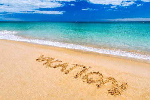 Vacation text on a beach. Vacation written in a sandy tropical beach. "Vacation" written in the sand on the beach blue waves in the background. Vacation on the sand beach concept.