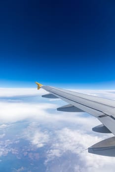 View of the wing of an airplane flying above the clouds at high altitude under a blue sky from the passenger window. In flight over Europe. View of jet airplane wing flying in blue sky over clouds.