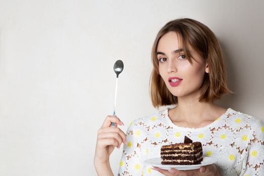 Thoughtful brunette woman holding sweet chocolate cake with cream. Empty space