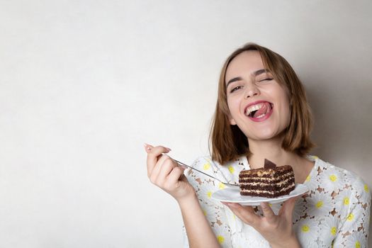 Happy grimacing woman eats tasty chocolate cake over a grey background. Empty space