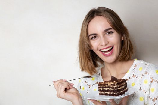 Cheerful woman holding a plate with tasty chocolate cake over a grey background. Empty space