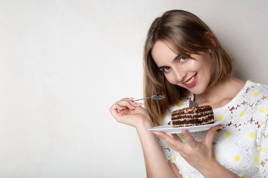 Flirty woman holding a plate with a tasty chocolate cake over a grey background. Empty space