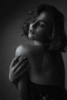 Glorious brunette woman posing in dark studio with closed eyes. Monochrome color