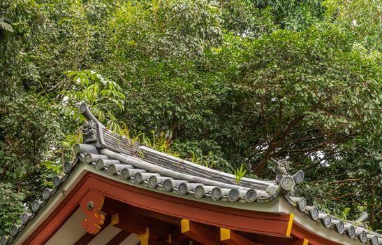Kaneohe, Oahu, Hawaii, USA. - January 11, 2020: Gray Roof decorations above red beams of Byodo-In Buddhist temple. Greeen foliage background.