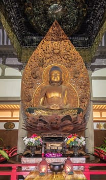 Kaneohe, Oahu, Hawaii, USA. - January 11, 2020: Golden Buddha in lotus position statue in Byodo-In Buddhist temple with backdrop and baldachin. Flowers in front.