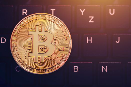 Bitcoin on compuer keyboard in background, symbol of electronic virtual money and mining cryptocurrency concept. Coin crypto currency bitcoin lies on the keyboard. Bitcoin on keyboard.