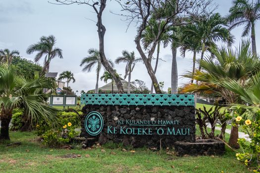 Kahului, Maui,, Hawaii, USA. - January 12, 2020: Native language sign for University of Hawaii, Maui college campus, set in green foliage and flower park along W. Kaahumanu Ave. Light blue sky.