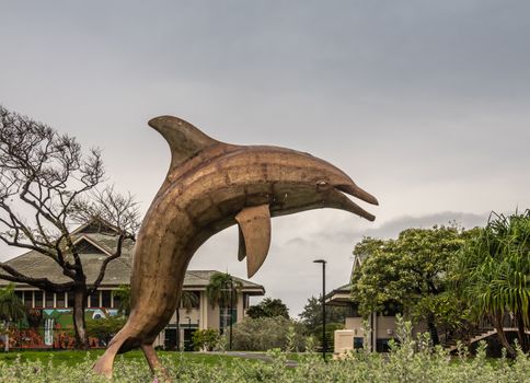 Kahului, Maui,, Hawaii, USA. - January 12, 2020: Dolphin statue on green lawn at University of Hawaii, Maui college campus. Gray cloudy sky. Class buildings and green foliage in back.