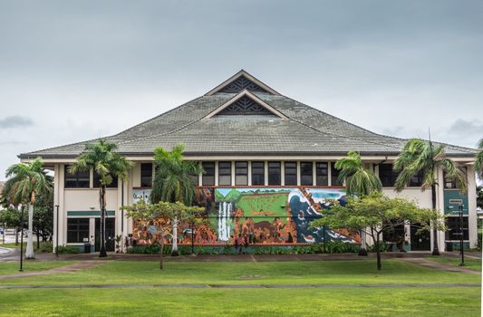 Kahului, Maui,, Hawaii, USA. - January 12, 2020: Big hall or Kaaike behind green lawn and under light blue sky at University of Hawaii, Maui college campus. Big wall painting featuring brown aboriginals.