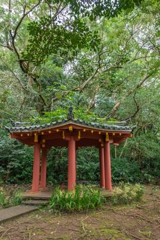 Kaneohe, Oahu, Hawaii, USA. - January 11, 2020: Small mediation pavilion with maroon pillars in garden of Byodo-In Buddhist temple. Greeen foliage background.