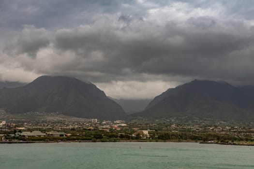 Kahului, Maui,, Hawaii, USA. - January 13, 2020: 2 black mountains tower over cityscape under heavy thick cloudscape full of rain. Azure ocean up front.