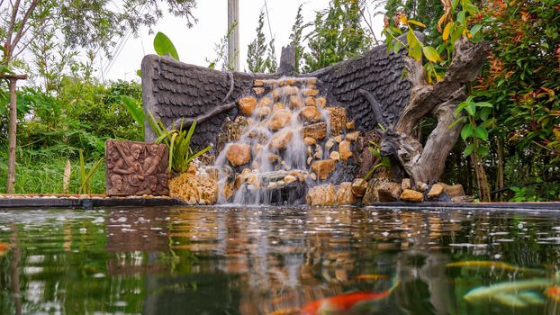 Fish pond with waterfall fountain. Garden waterfall landscaping with fishes, rocks, flowers and plants.