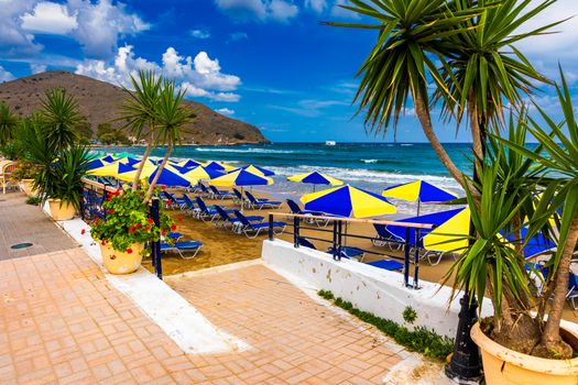 Summer vacation destination. Straw sunshades and sunbeds on the empty pebble beach with sea in the background. Vacation And Tourism Concept. Sunbeds On The Paradise Beach. Umbrellas and sunbeds.