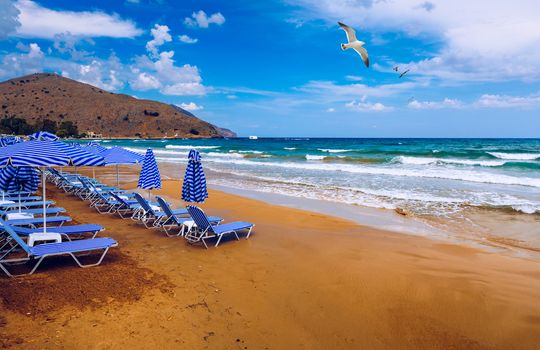 Summer vacation destination. Straw sunshades and sunbeds on the empty pebble beach with sea in the background. Vacation And Tourism Concept. Sunbeds On The Paradise Beach. Umbrellas and sunbeds.