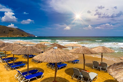 Summer vacation destination. Straw sunshades and sunbeds on the empty pebble beach with sea in the background. Vacation And Tourism Concept. Sunbeds On The Paradise Beach. Umbrellas and sunbeds.